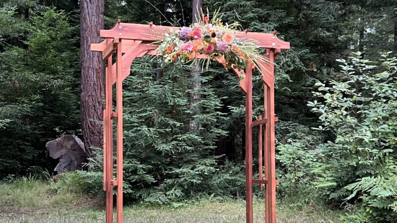 Wooden wedding arch from Mitchell Grove lending closet decorated with a single floral accent, zip-tied by friends as a DIY budget hack.