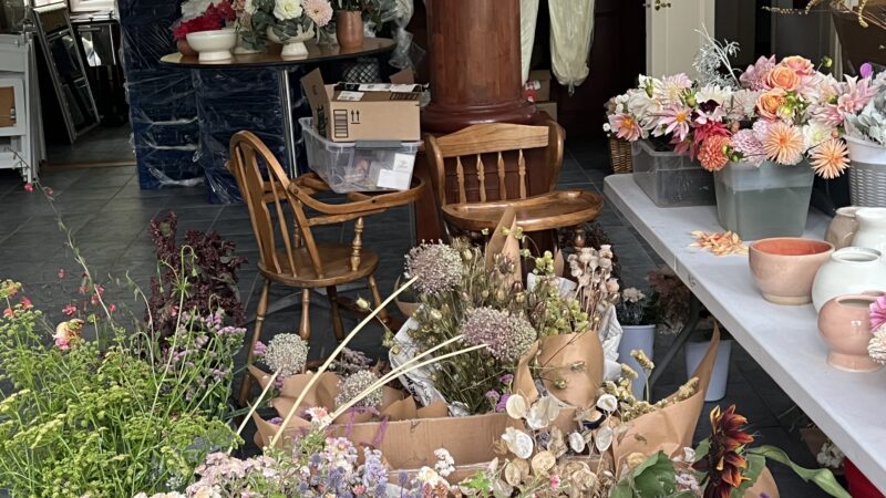 Wedding flower workshop in the hall with buckets of blooms, chairs, and tables filled with centerpieces in progress.