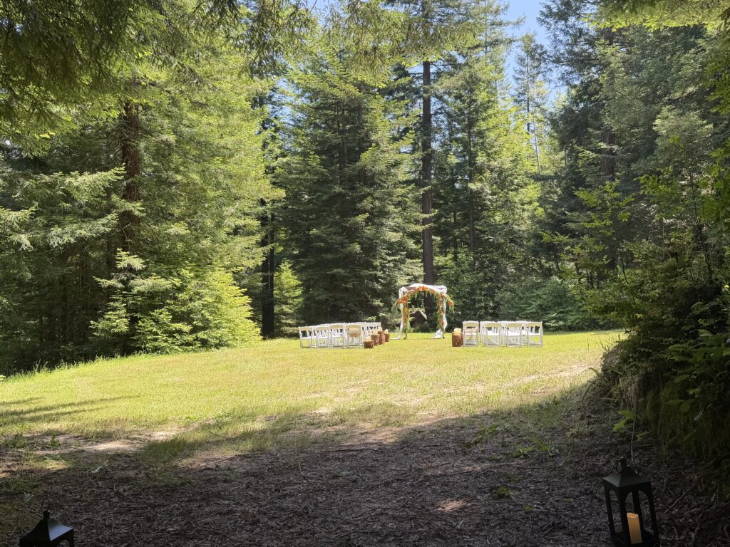 Private redwood forest wedding ceremony area with white chairs, decorated arch, and redwood trees surrounding a peaceful clearing in Humboldt County.