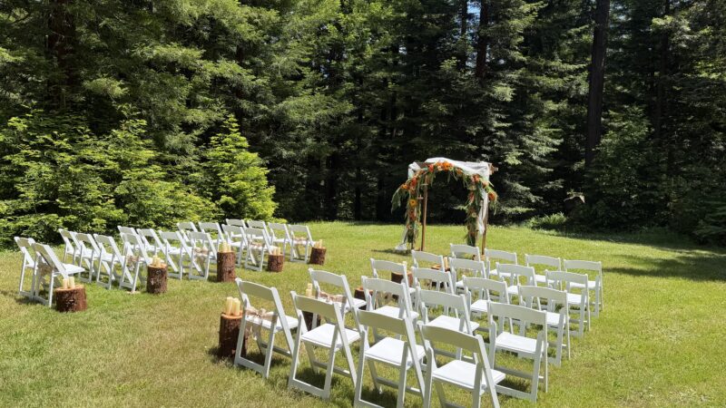 Wedding ceremony setup in a redwood forest clearing at Mitchell Grove, featuring white chairs, redwood rounds, and an arch for a DIY wedding in Humboldt County.